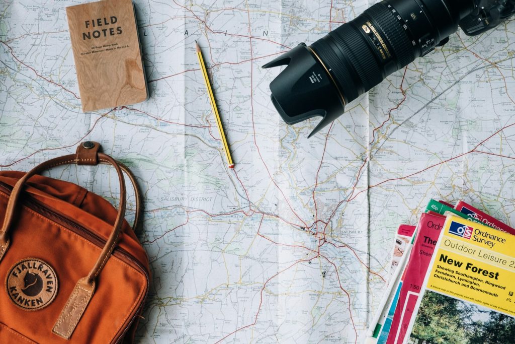 A travel map, camera, notebook and bag laid out on a table