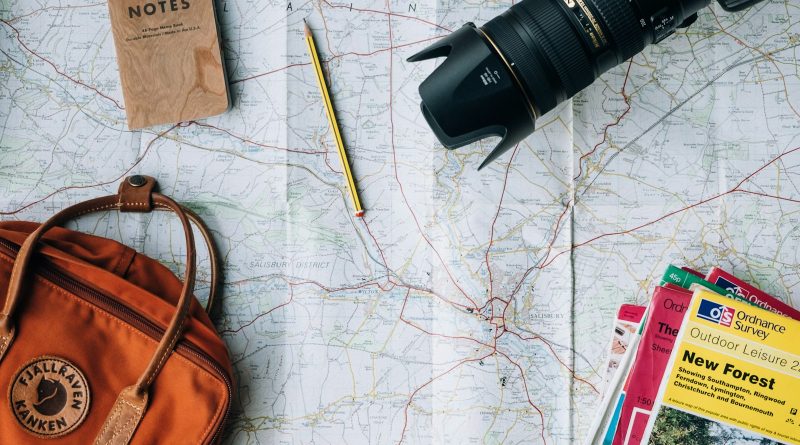 A travel map, camera, notebook and bag laid out on a table