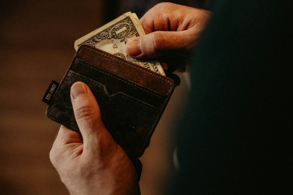 A hand placing a banknote into a leather wallet