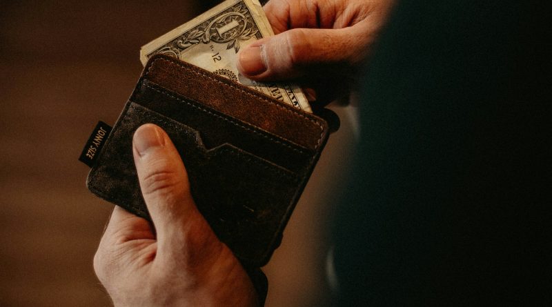 A hand placing a banknote into a leather wallet