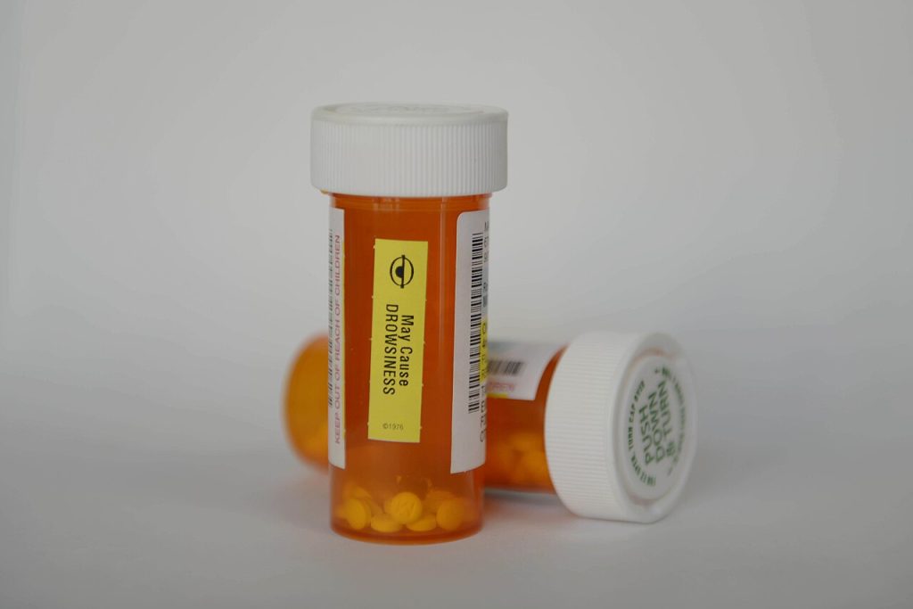 Two orange prescription pill bottles with white caps, one labeled with a warning that it may cause drowsiness.