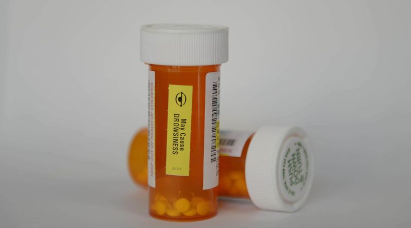 Two orange prescription pill bottles with white caps, one labeled with a warning that it may cause drowsiness.